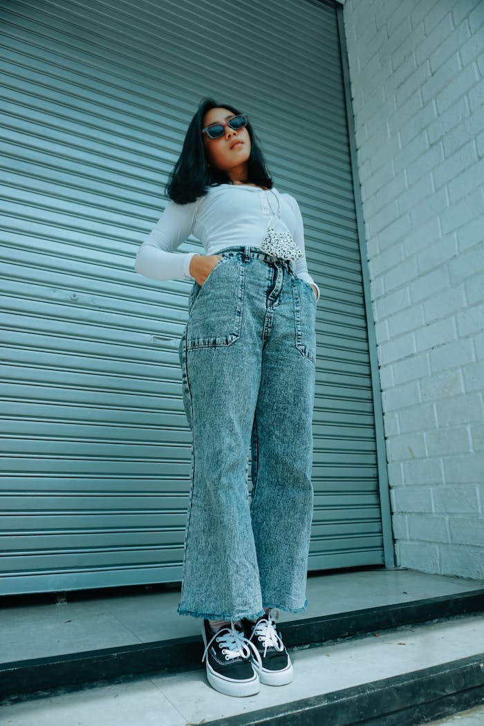 Low angle of Asian woman in casual outfit standing on cemented stairs near wall with geometric ornament